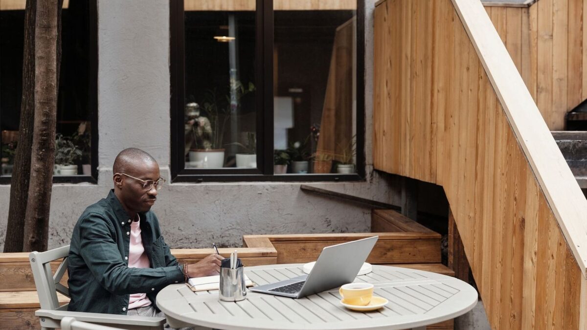 Person skriver vid laptop och kaffe på en lugn uteservering