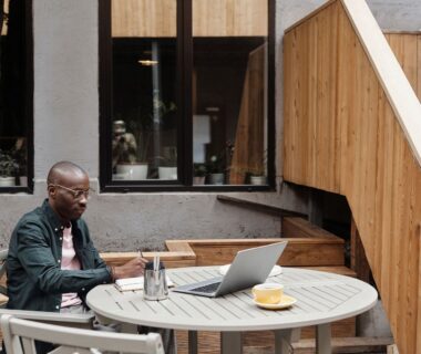 Person skriver vid laptop och kaffe på en lugn uteservering