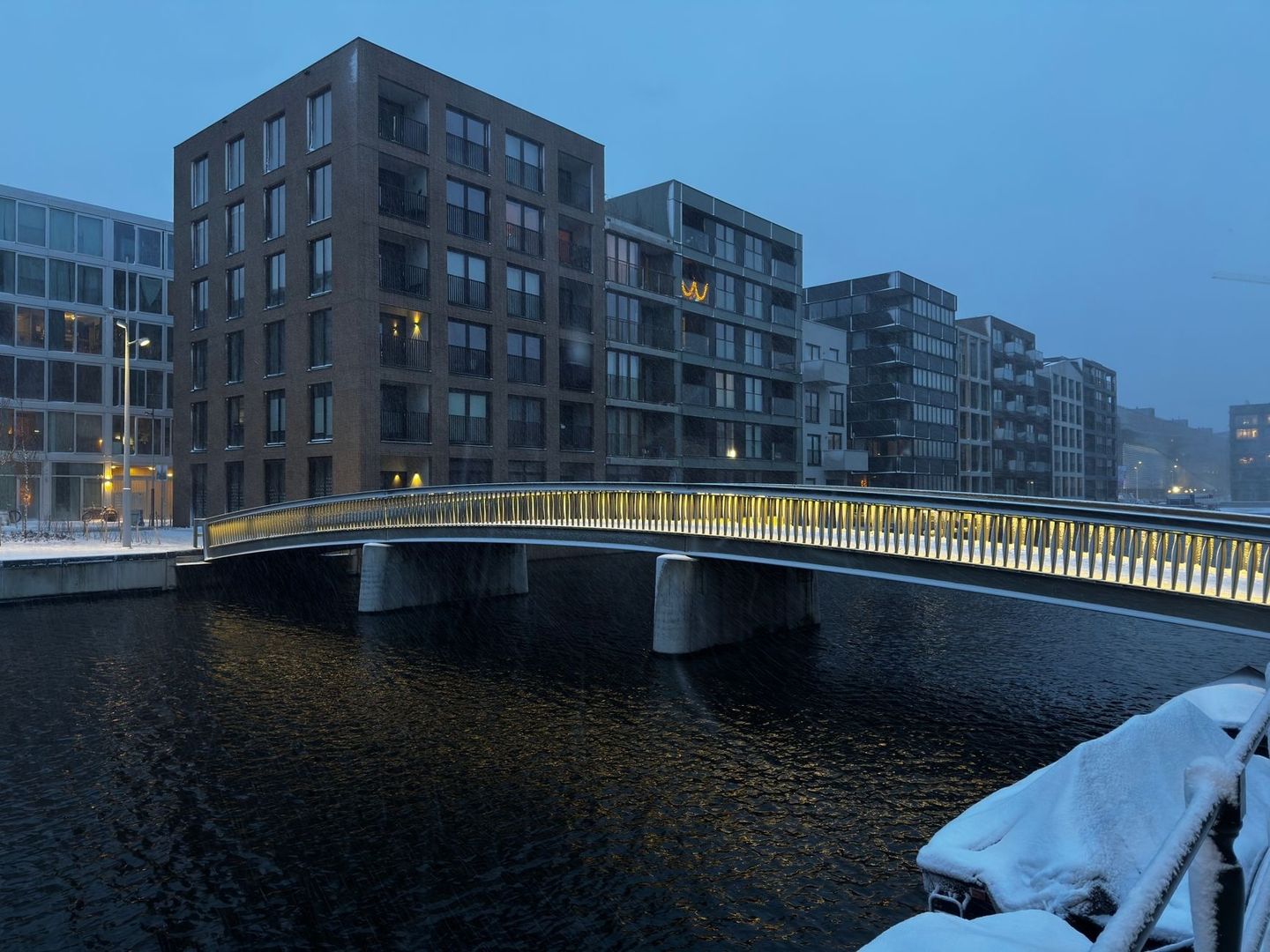 Snötäckt gångbro över kanalen vid Hammarby sjöstad i skymningen